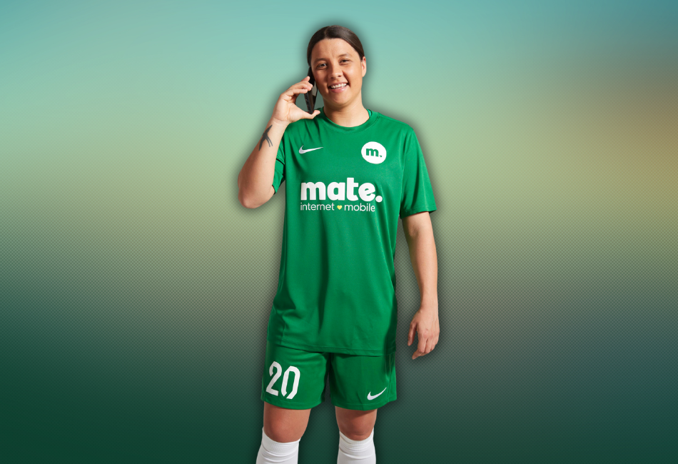 Soccer Captain Sam Kerr is standing, taking a phone call while wearing a soccer jersey and shorts featuring the MATE logo.