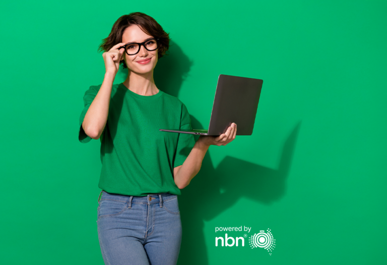 person holding laptop, adjusting glasses in front of green backdrop by nbn